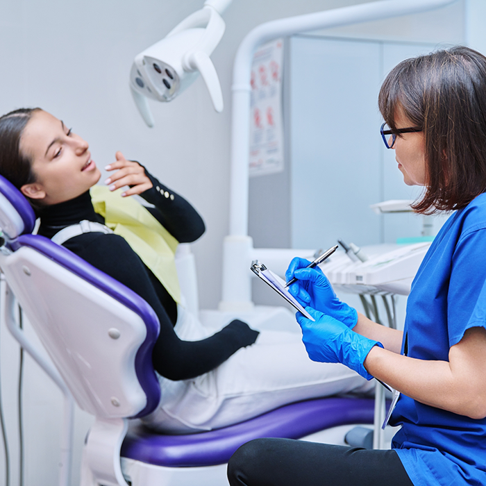 Dentist writing on a clipboard while talking to a patient in the treatment chair