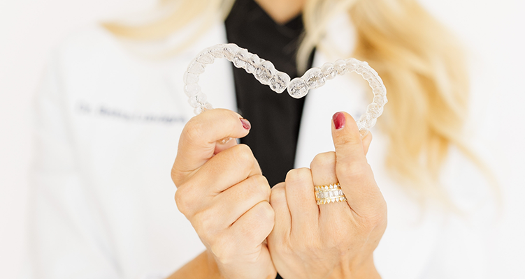 Dentist holding two Invisalign clear aligners in Wilmington in a heart shape