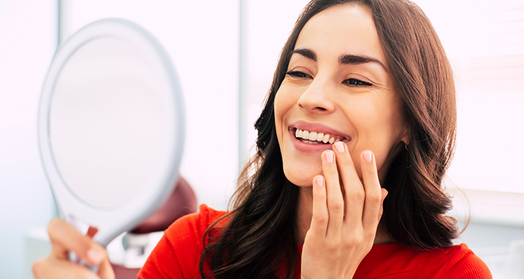 Woman looking at her smile in a mirror after replacing missing teeth in Wilmington