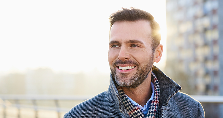 Man in a gray coat smiling in the sun after restorative dentistry in Wilmington