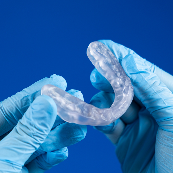 Gloved hands holding a clear occlusal splint tray